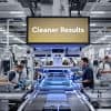 People working on a factory floor with UV curing equipment and a digital sign reading 'Cleaner Results'